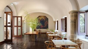 A dining area with wooden tables and chairs, a large painting on the wall, and a stone column. - Convento do Espinheiro, Historic Hotel & Spa (Évora)
