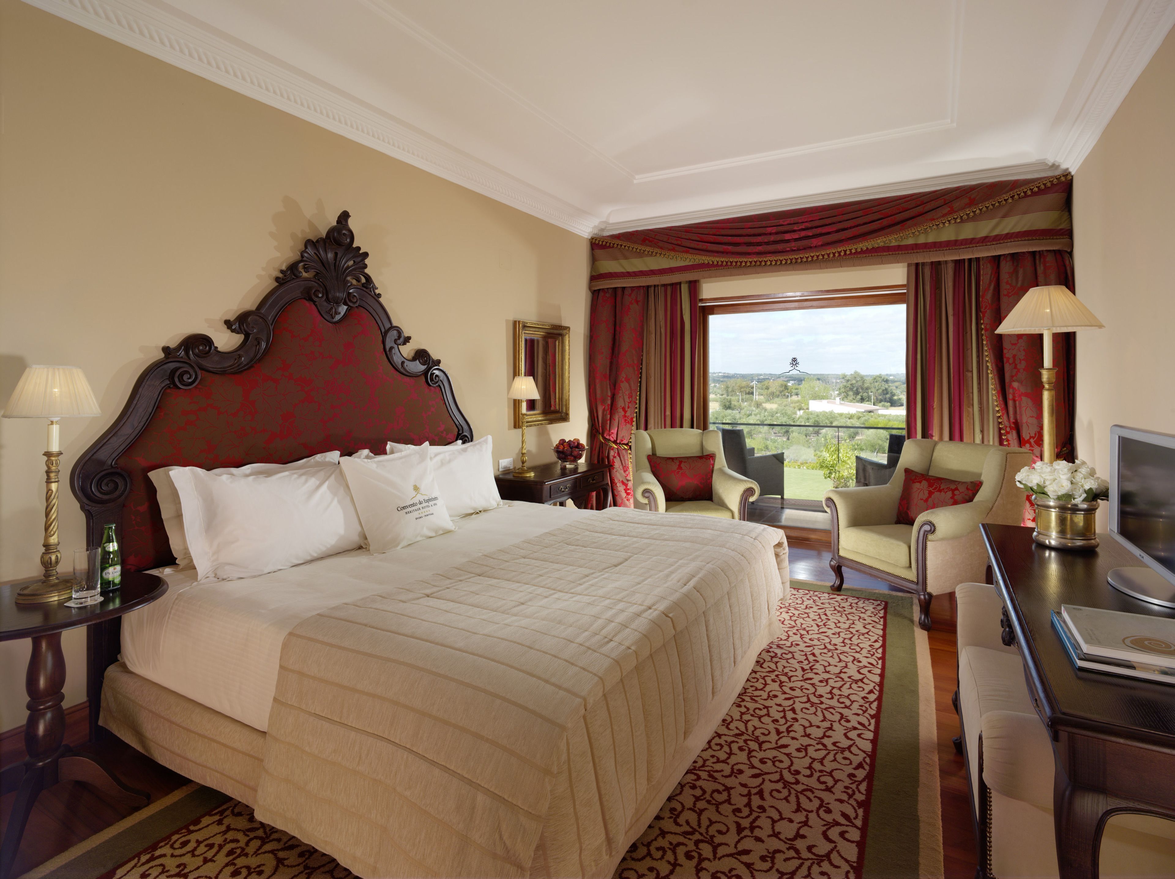 A hotel room with a large bed, two armchairs, a desk, and a view of the outdoors.