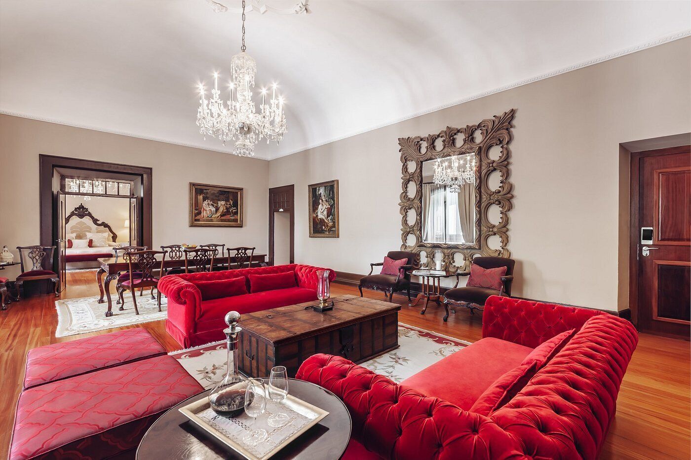 Un salón amplio con un juego de sofá rojo, una araña y un espejo grande y ornamentado.
