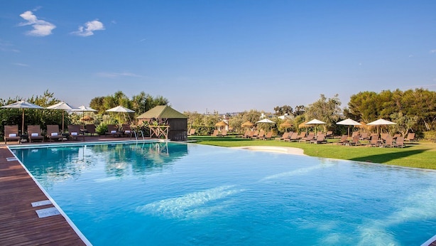 A swimming pool with lounge chairs and umbrellas, surrounded by greenery. - Convento do Espinheiro, Historic Hotel & Spa (Évora)