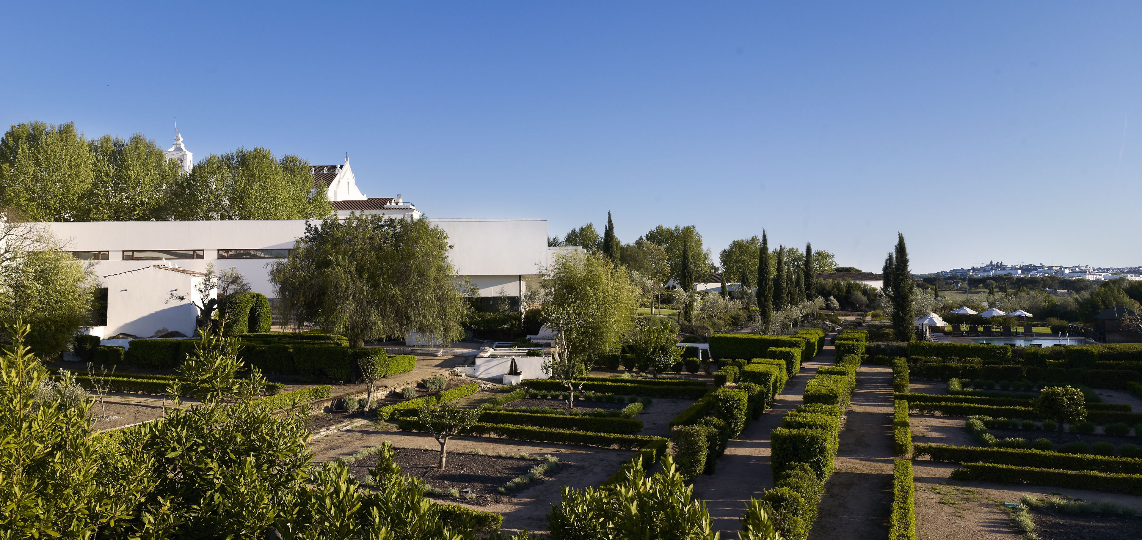 Un jardín formal con setos podados y un edificio blanco con una cúpula al fondo.