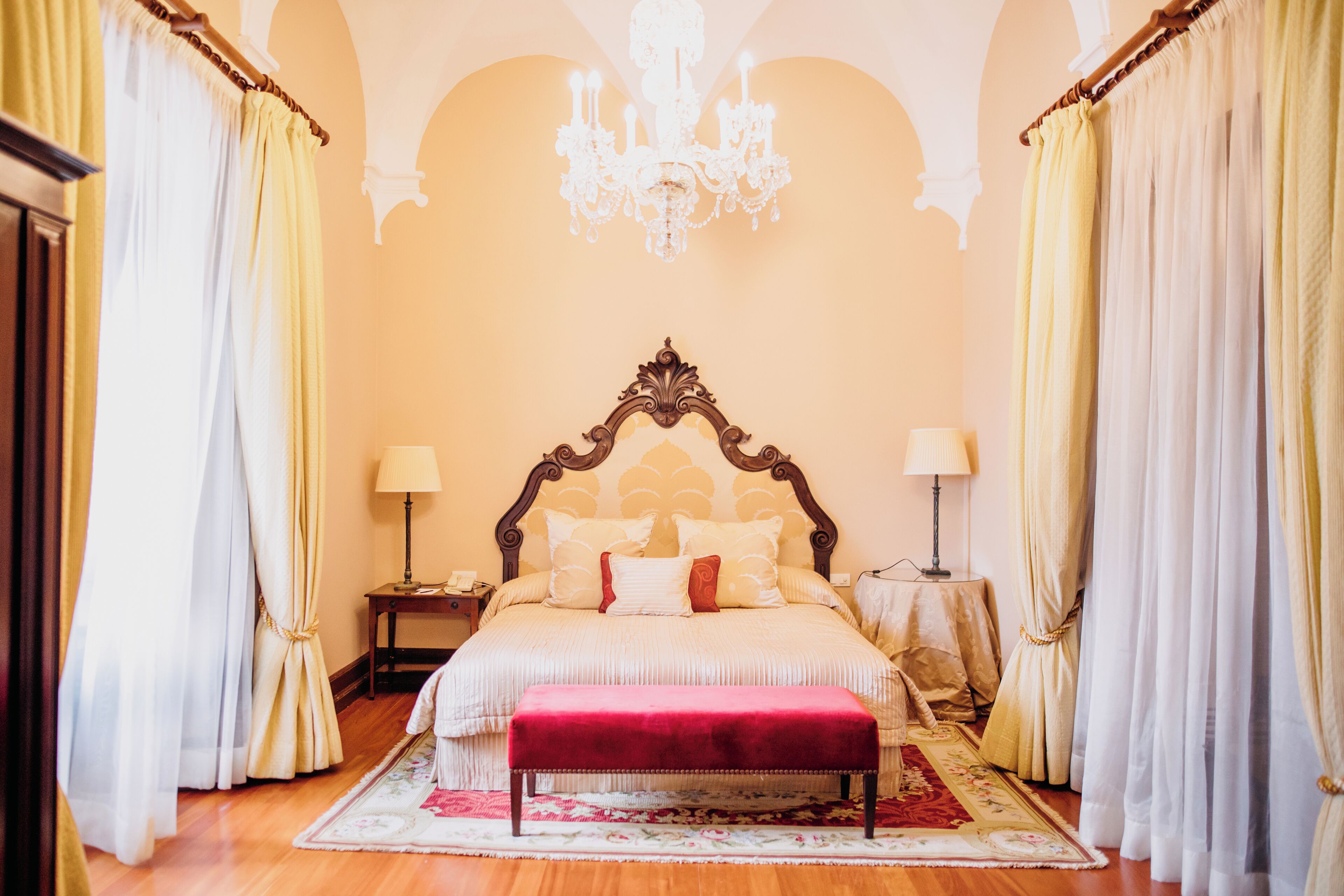 Quarto com uma cama grande, um candelabro, cortinas e piso de madeira.
