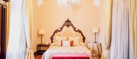 A bedroom with a large bed, a chandelier, curtains, and a wooden floor.