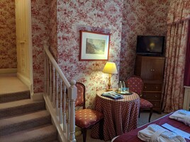 Una habitación de hotel con una escalera, una mesa con mantel a cuadros, una lámpara, un televisor y un armario.