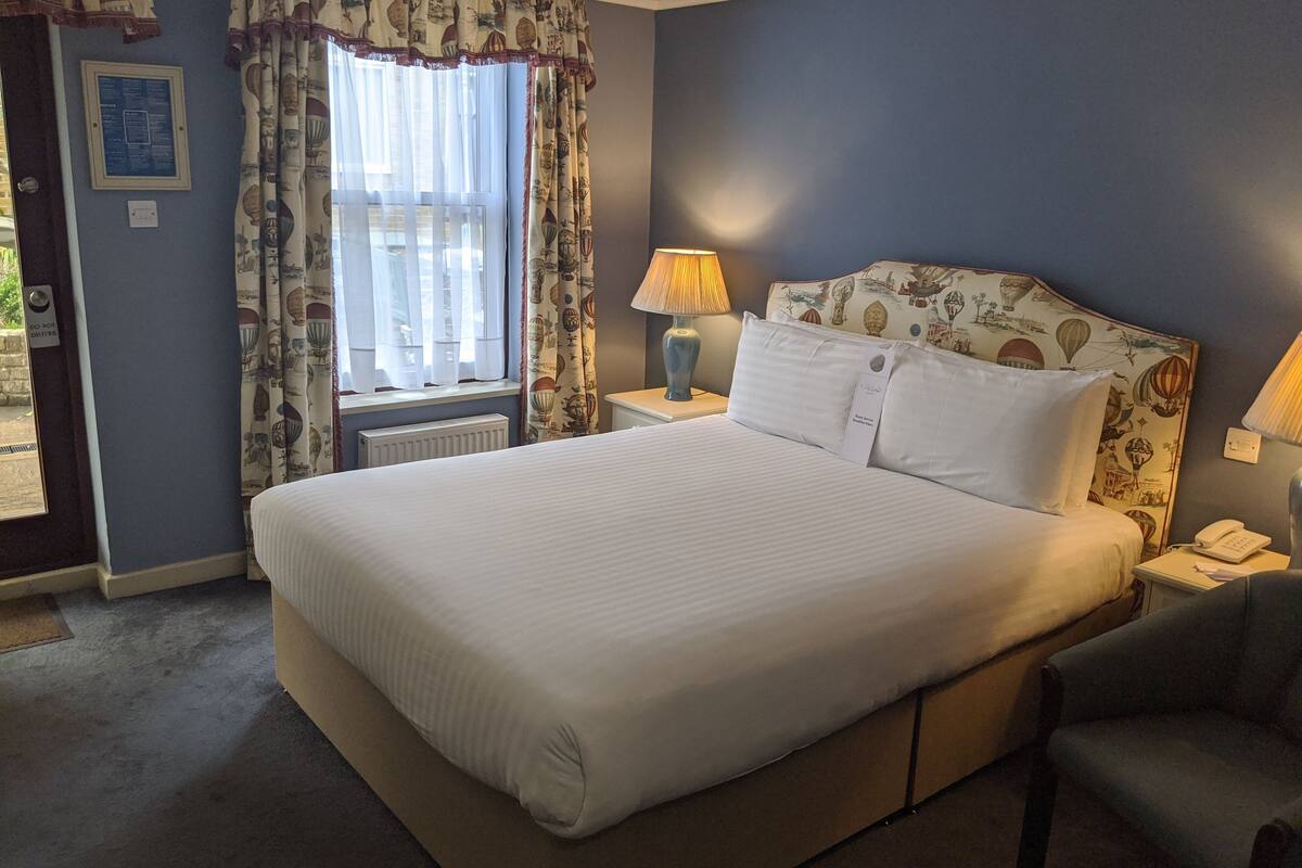 A neatly made bed with white linens, a nightstand with a lamp, and a chair.