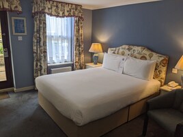 A neatly made bed with white linens, a nightstand with a lamp, and a chair.
