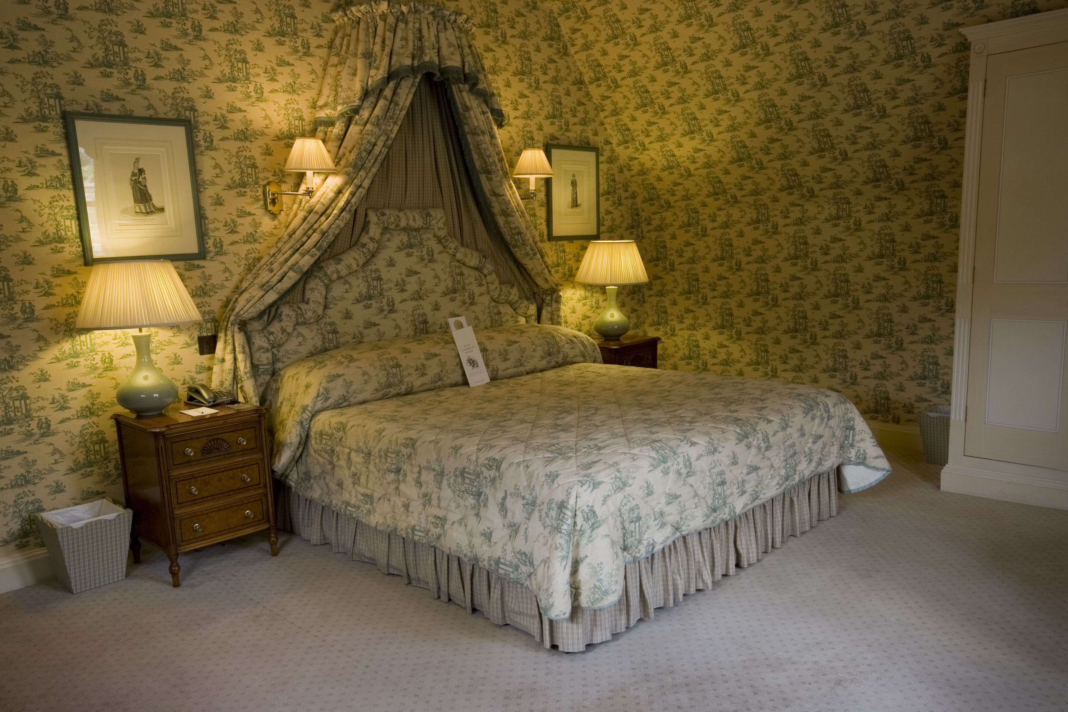 A bedroom with a canopy bed, two bedside lamps, a nightstand, and a framed picture on the wall.
