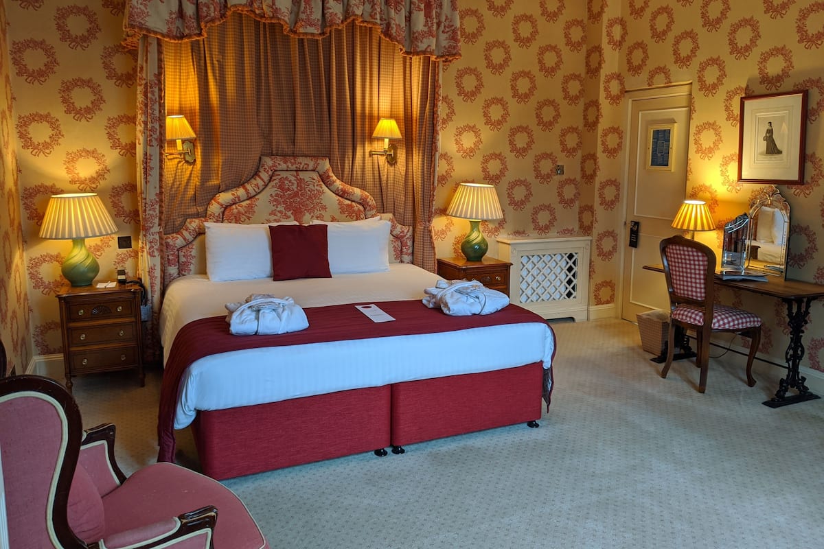 A hotel room with a large bed, two bedside lamps, a desk with a chair, and a wardrobe.