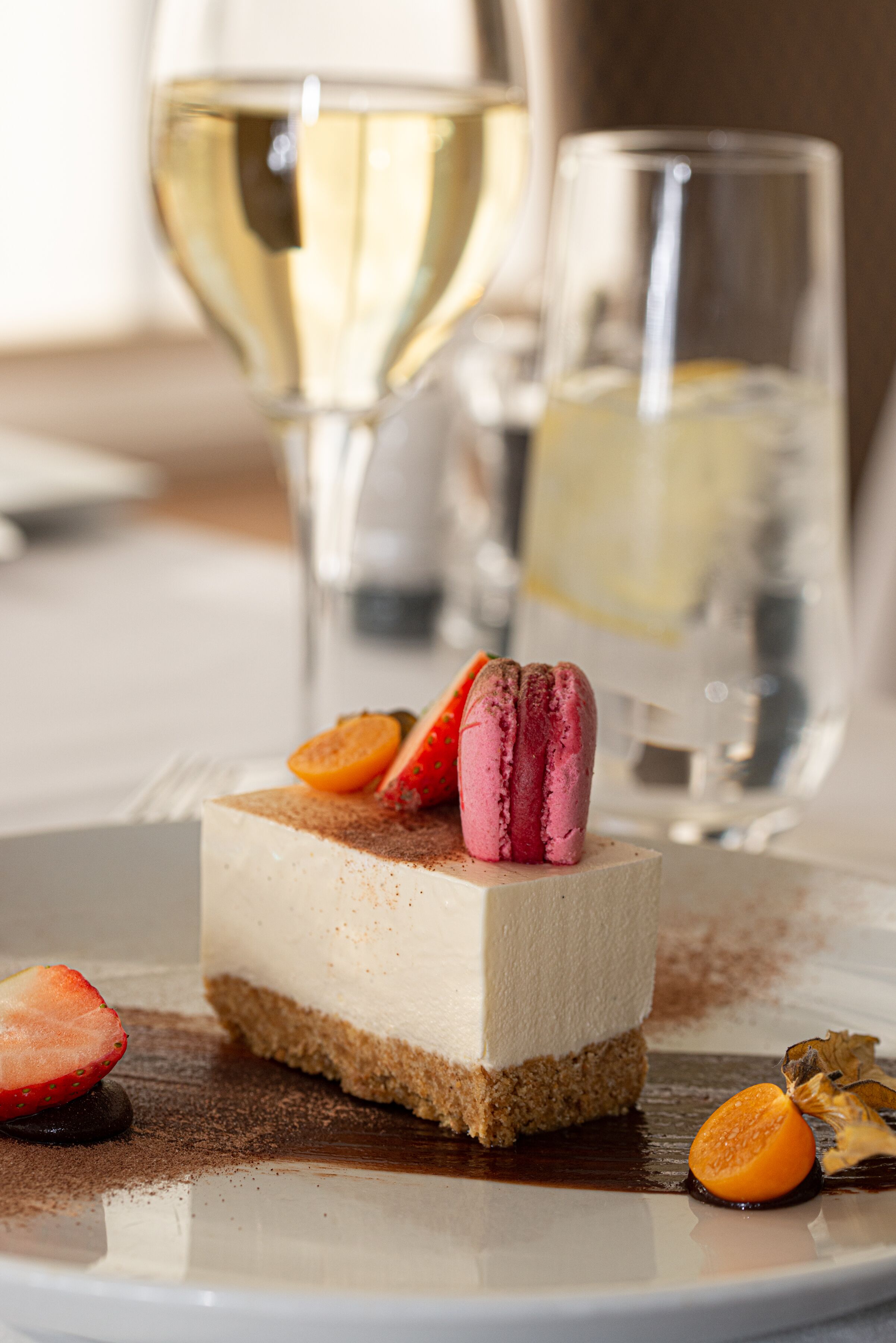 Ein Dessert mit Macarons und Früchten auf einem Teller, dazu ein Glas Weißwein.