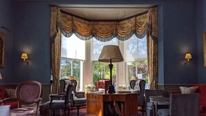 A room with a large window, a desk with a lamp, and several chairs. - Cotswold Lodge Hotel (Oxford)