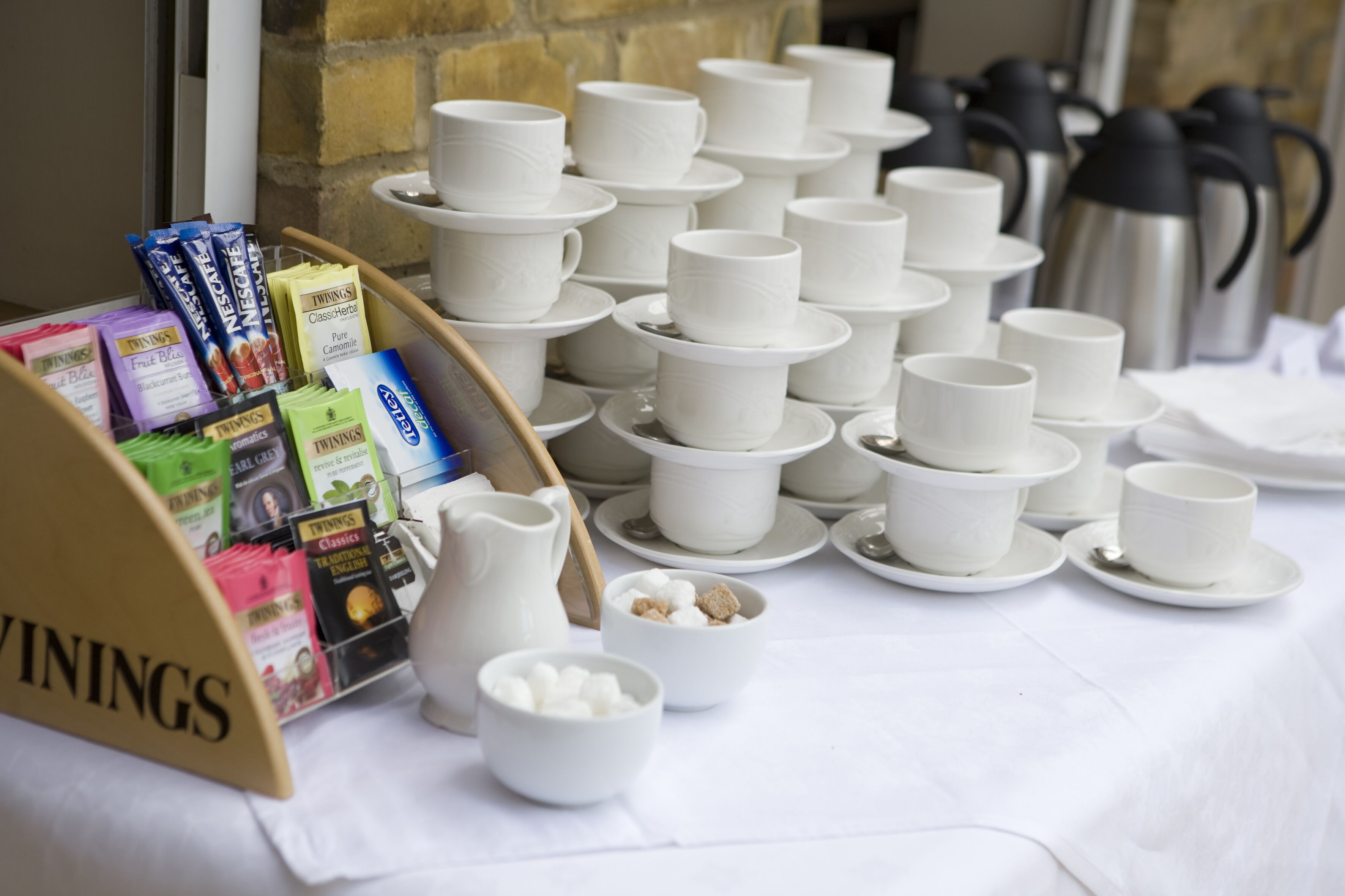 A table with white cups and saucers, a pitcher, and a bowl of sugar cubes.