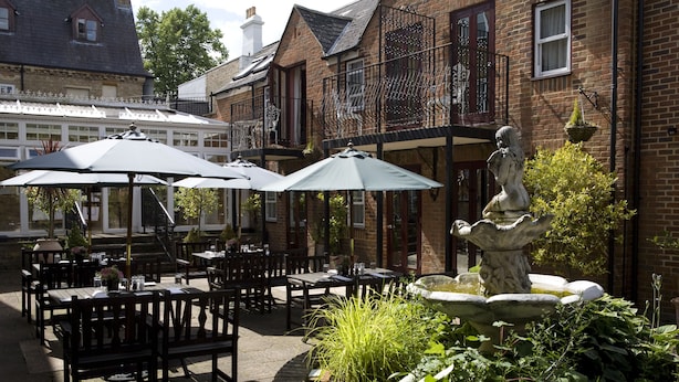 An outdoor patio area with tables and chairs, a stone fountain, and a statue. - Cotswold Lodge Hotel (Oxford)