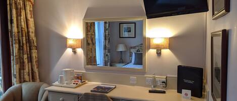 A hotel room with a desk, chair, and a television mounted on the wall.