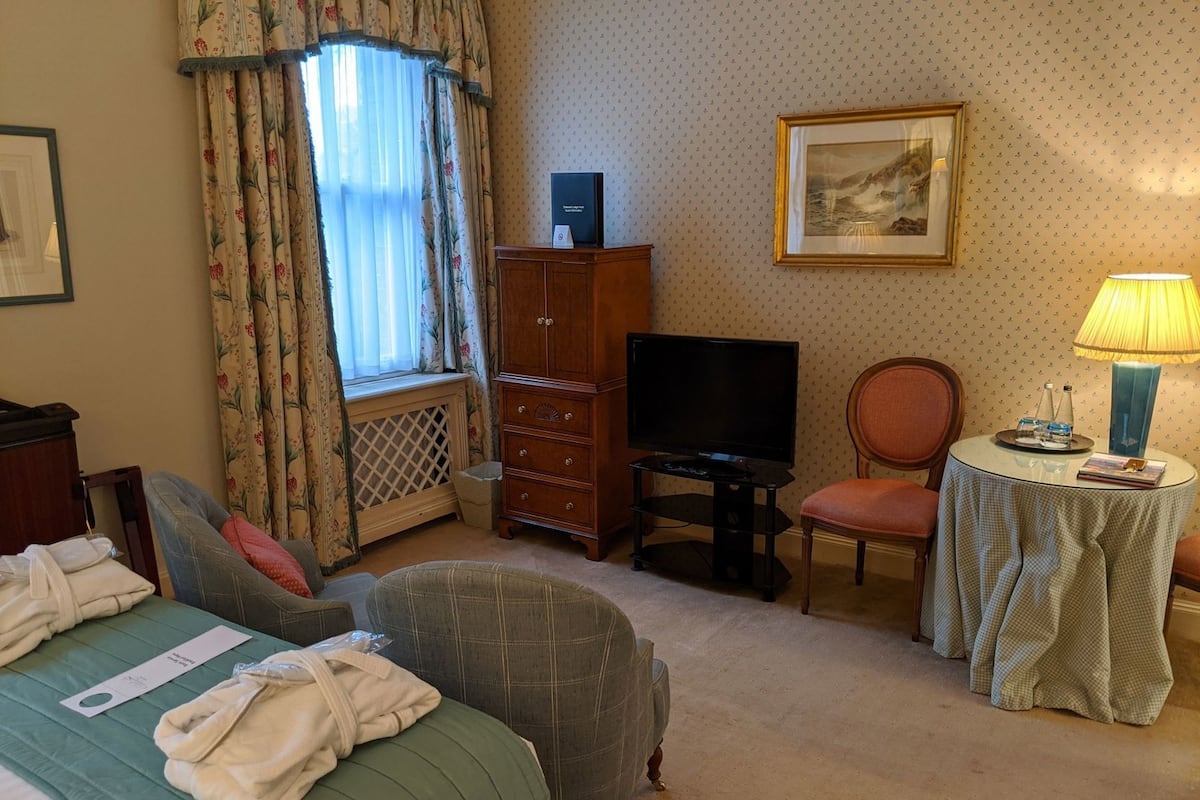 A hotel room with a bed, a television, a chair, a small table, and a lamp.