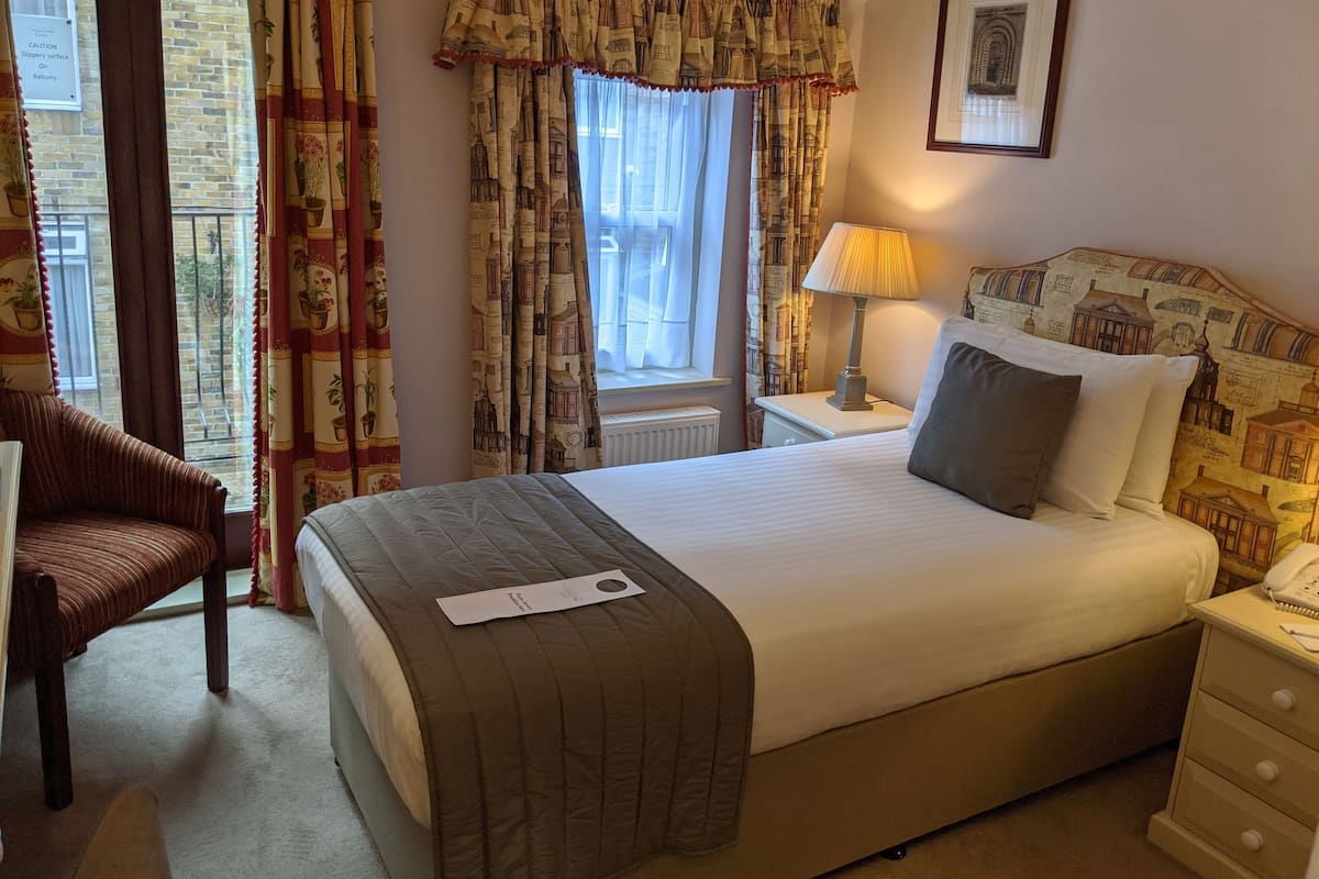 A hotel room with a bed, bedside table, lamp, and a chair.