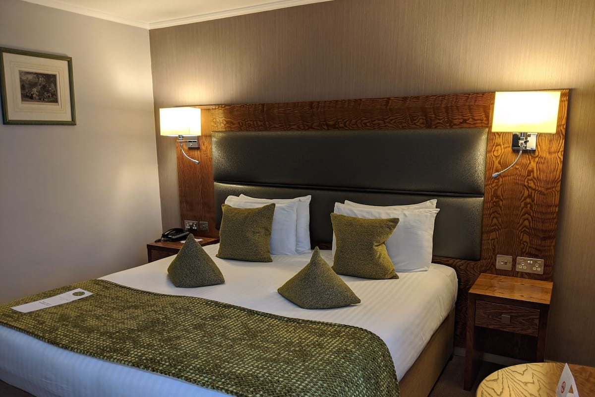 A hotel room with a large bed, a wooden headboard, and two bedside lamps.