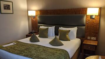Una habitación de hotel con una cama grande, un cabecero de madera y dos lámparas de noche.