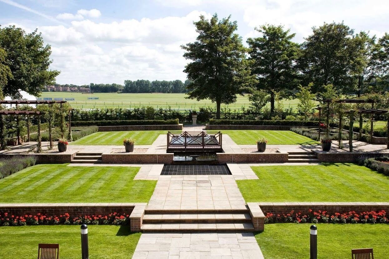 A well-maintained garden with a central water feature, surrounded by neatly trimmed grass and bordered by brick pathways.