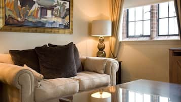 Una sala de estar con un sofá color beige, una mesa de centro de vidrio, una lámpara y un cuadro en la pared.
