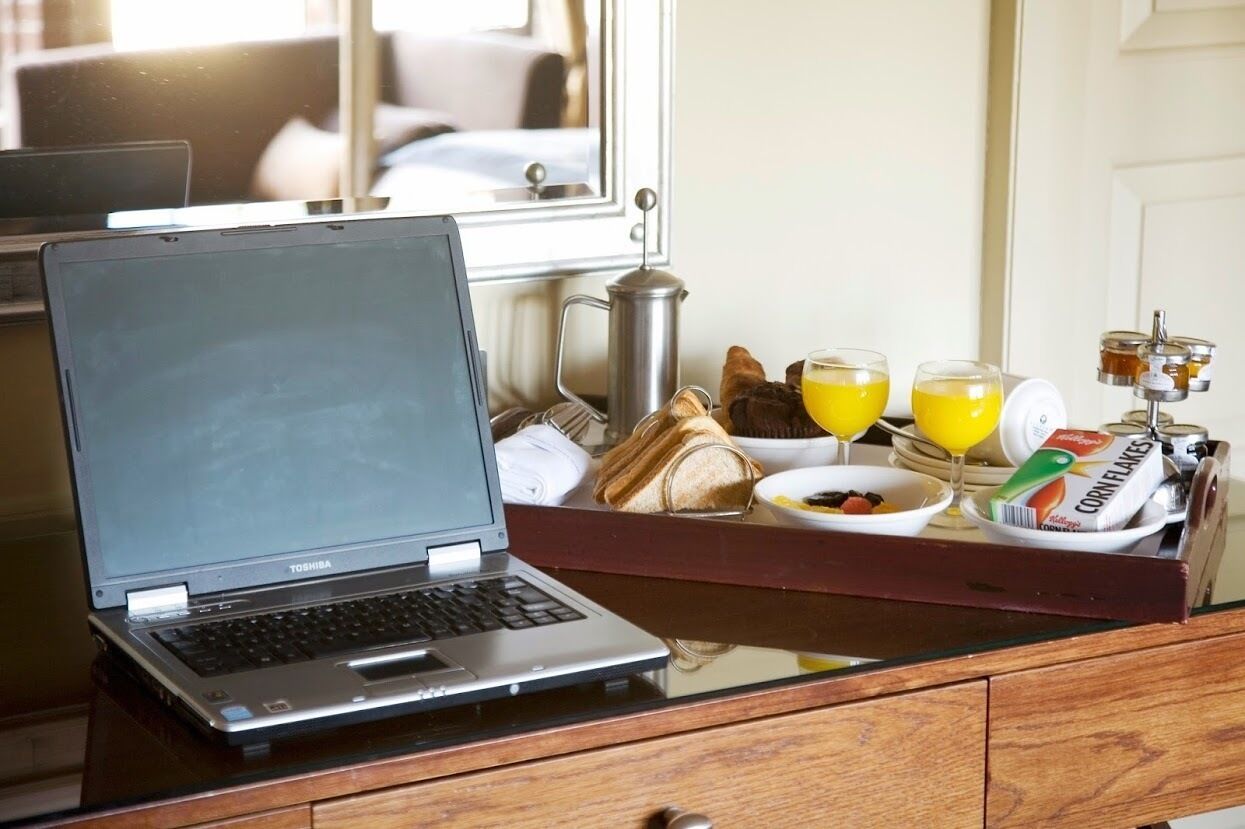 Una laptop Toshiba sobre una mesa de vidrio con alimentos para el desayuno, incluyendo pan, jugo y cereal.