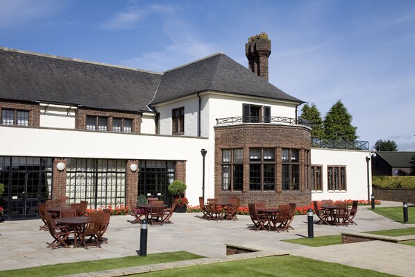 A building with a brick facade, large windows, and outdoor seating area with tables and chairs.