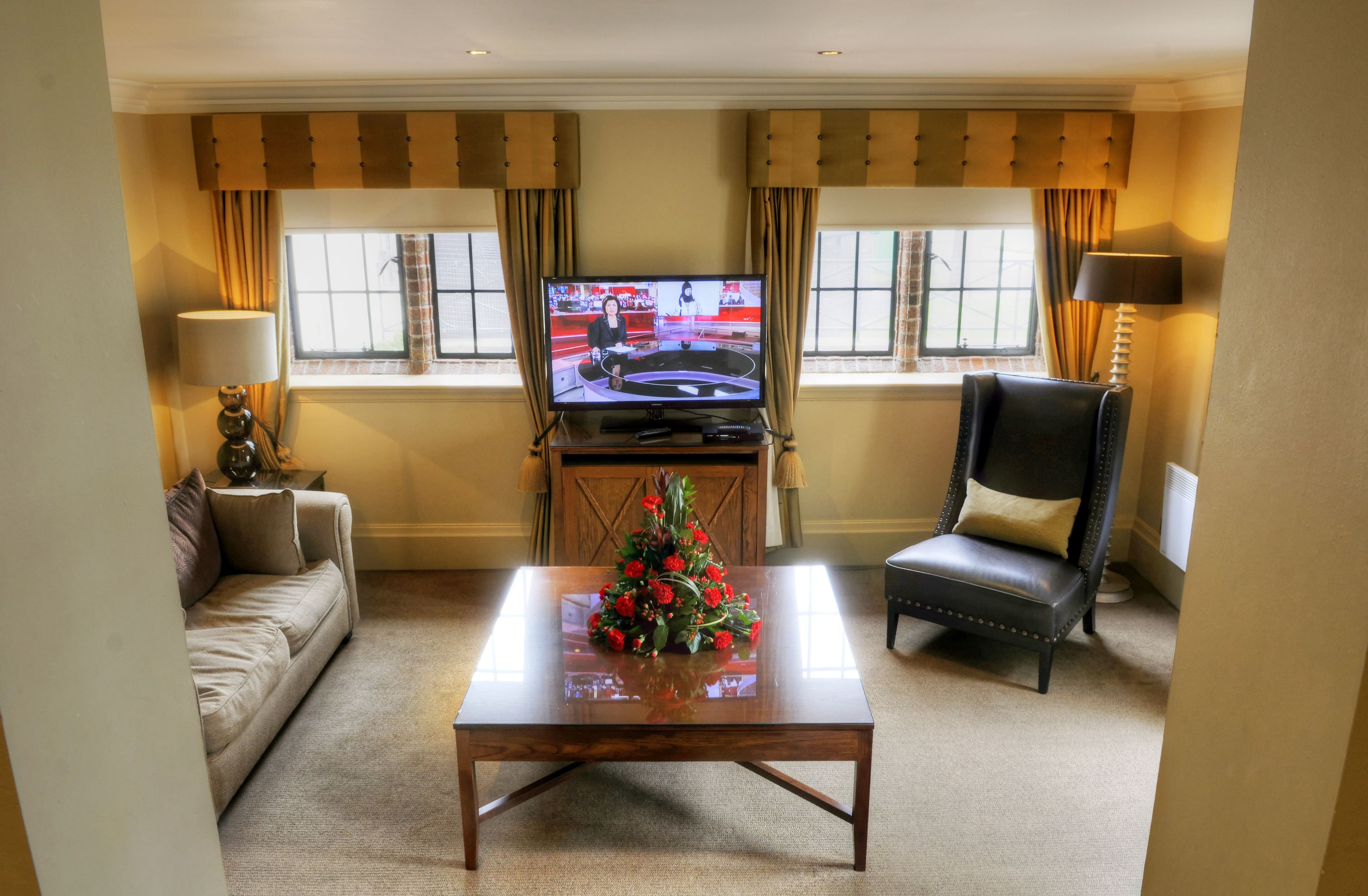 A living room with a television, a sofa, a coffee table with a floral centerpiece, a leather armchair, and a lamp.