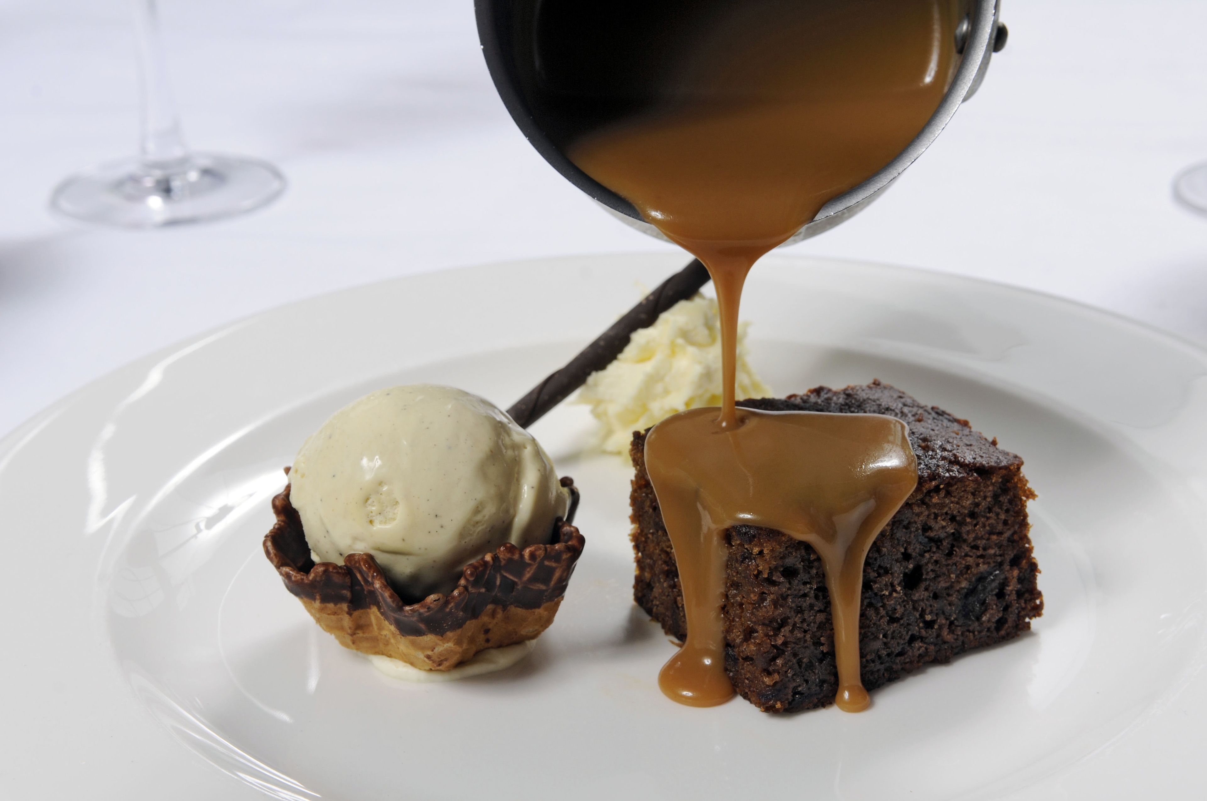 A dessert plate with a scoop of ice cream and a piece of cake drizzled with caramel sauce.