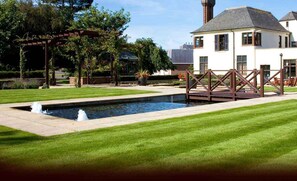 A well-maintained garden with a rectangular pool, a pergola, and a white building with a chimney. - Western House Hotel (Ayr)