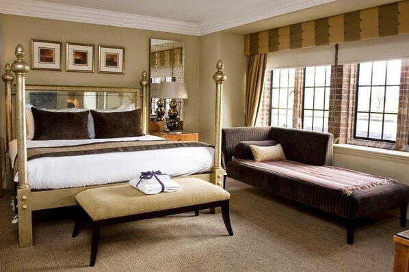 Habitación de hotel con una cama grande, un sofá, una banca y una ventana con cortinas.