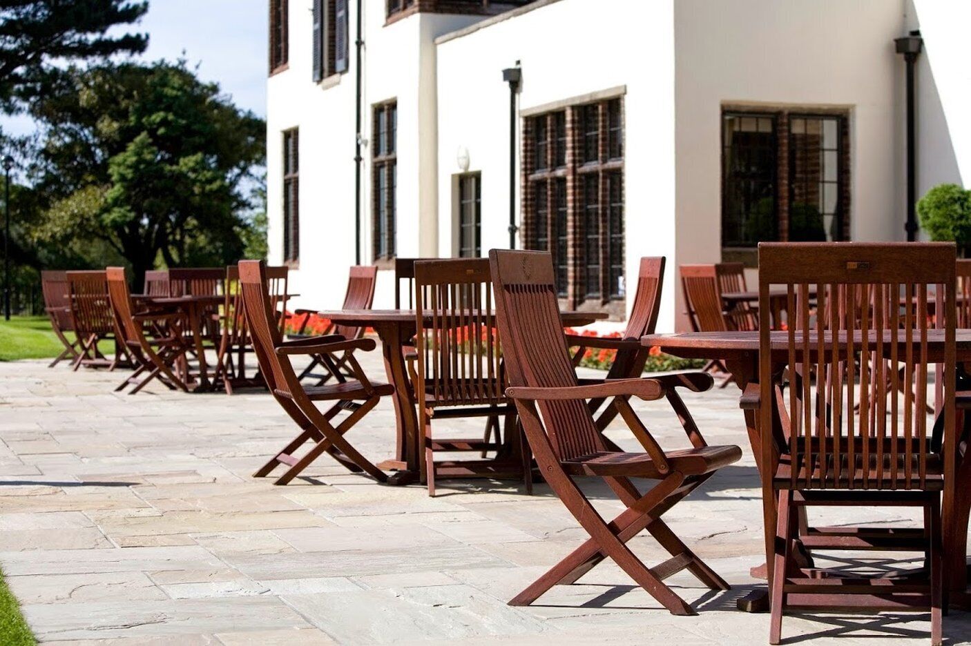 Outdoor wooden tables and chairs arranged on a stone patio.