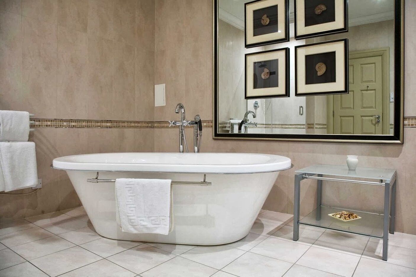 A bathroom with a freestanding bathtub, a small side table with a vase, and a large mirror above the tub.