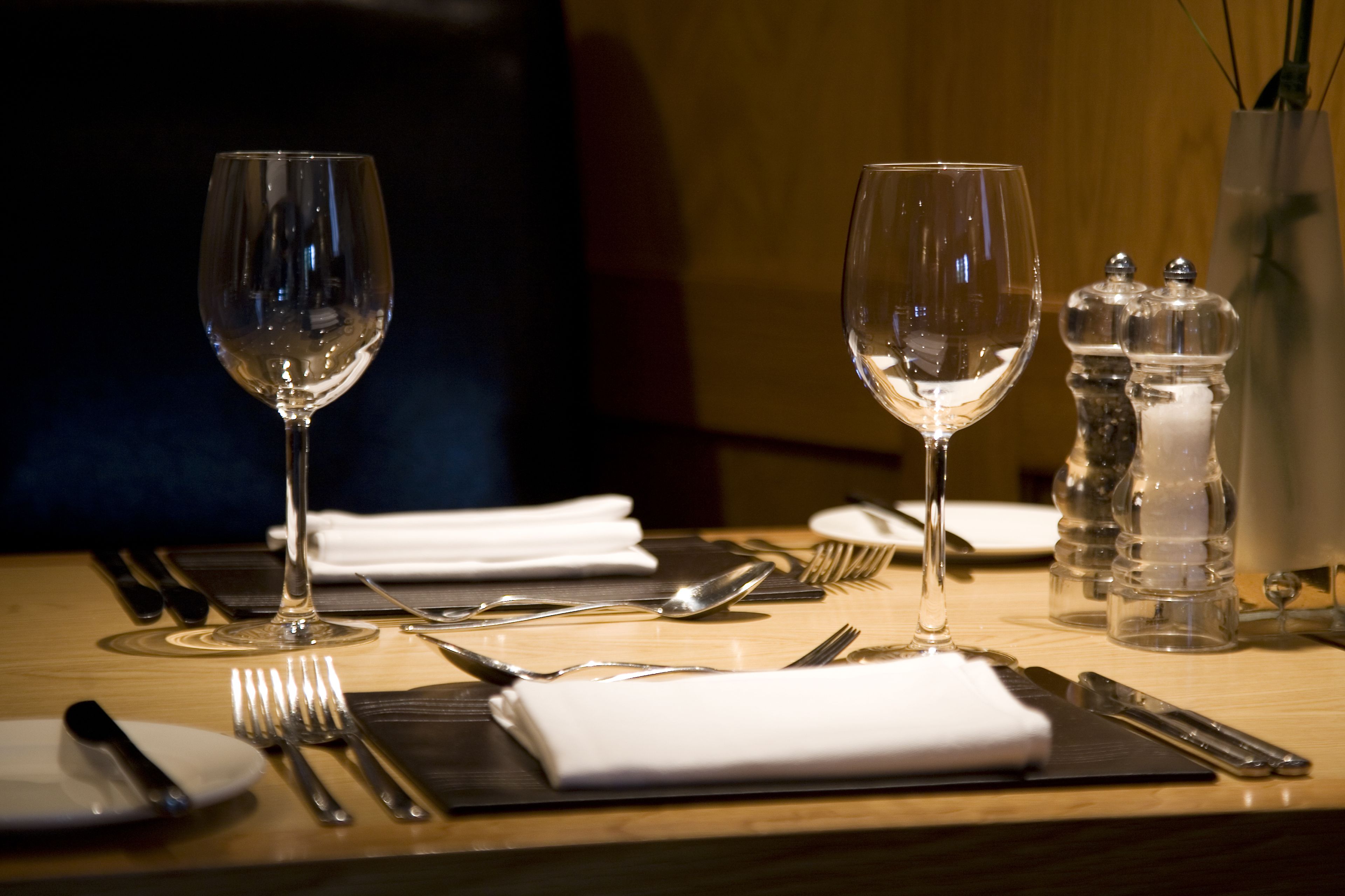 A dining table set with wine glasses, cutlery, plates, and salt and pepper shakers.