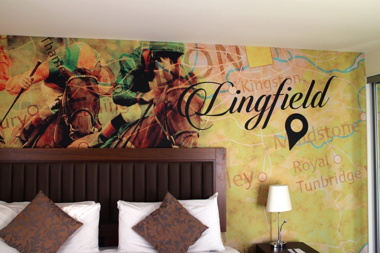 Een hotelkamer met een grote muurdecoratie van een kaart, een houten hoofdbord, twee witte kussens en een bedlampje.