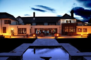 A large, two-story building with a central courtyard, outdoor seating area, and a small water feature.