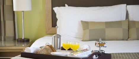 A neatly made breakfast tray on a bed with a pillow, a bedside lamp, and a nightstand with a lamp.