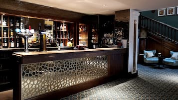 A bar area with a patterned floor, wooden counter, and shelves of bottles.