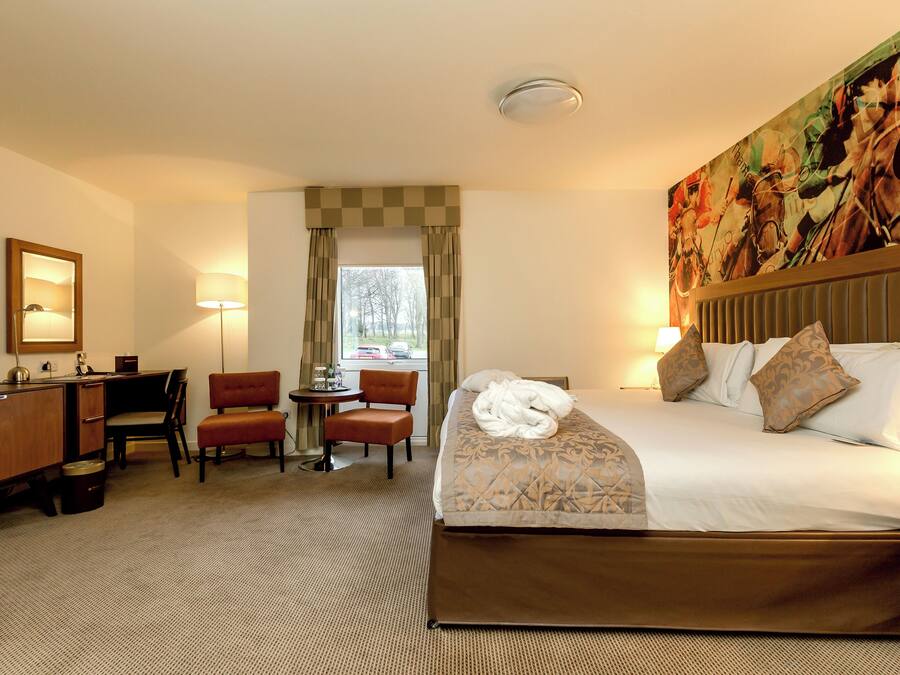 Una habitación de hotel con cama, escritorio, silla, televisión y ventana con cortinas.
