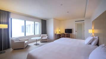 Habitación de hotel con una cama grande, un escritorio, una silla, un televisor y una ventana con cortinas.