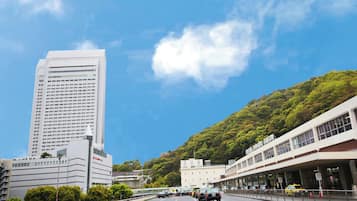 A multi-story building with a modern architectural design, adjacent to a lush green hillside.