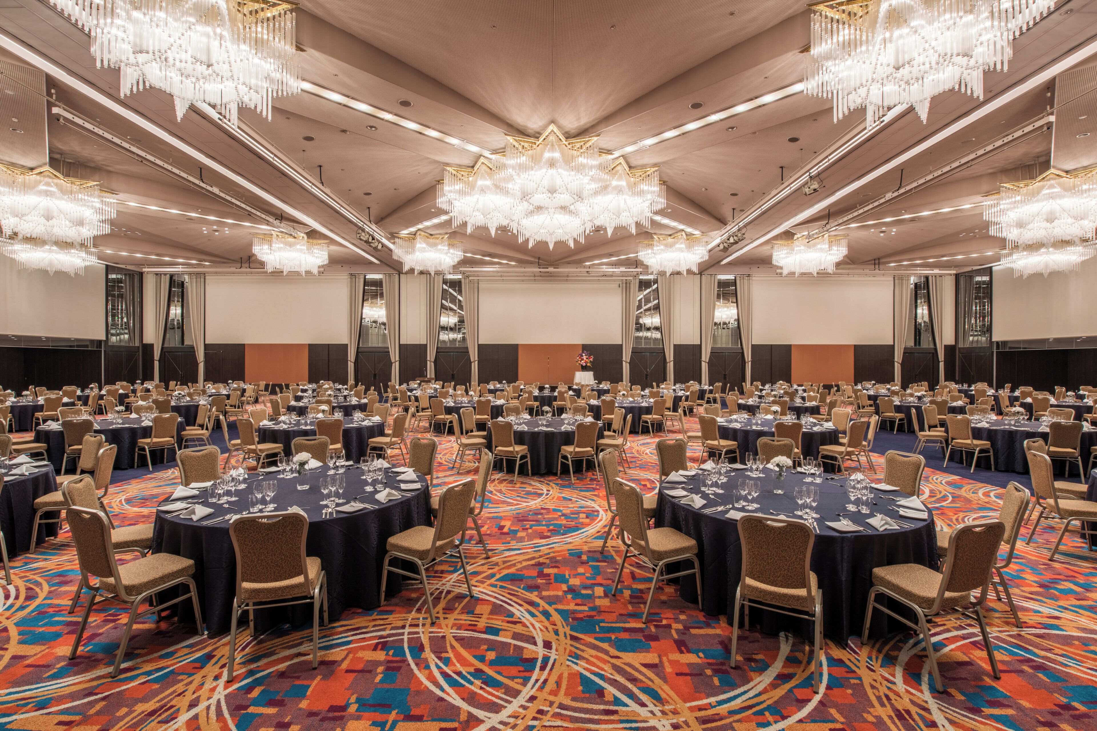 Une grande salle de banquet avec des tables rondes, des chaises et un tapis à motifs.