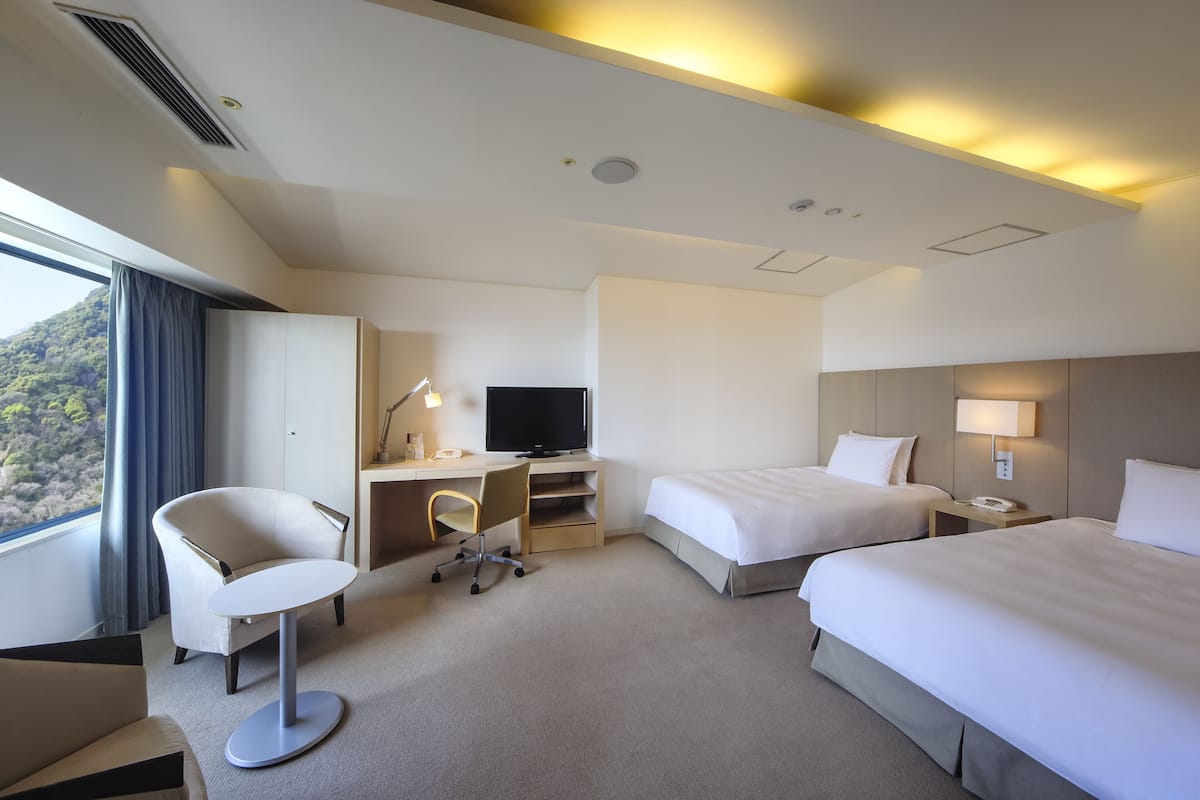 A hotel room with two beds, a desk with a computer, a chair, and a TV.