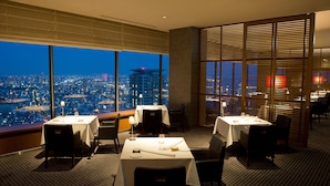 A dining area with tables set for two, large windows offering a city view, and a partition with blinds. - ANA Crowne Plaza Kobe by IHG (Kobe)