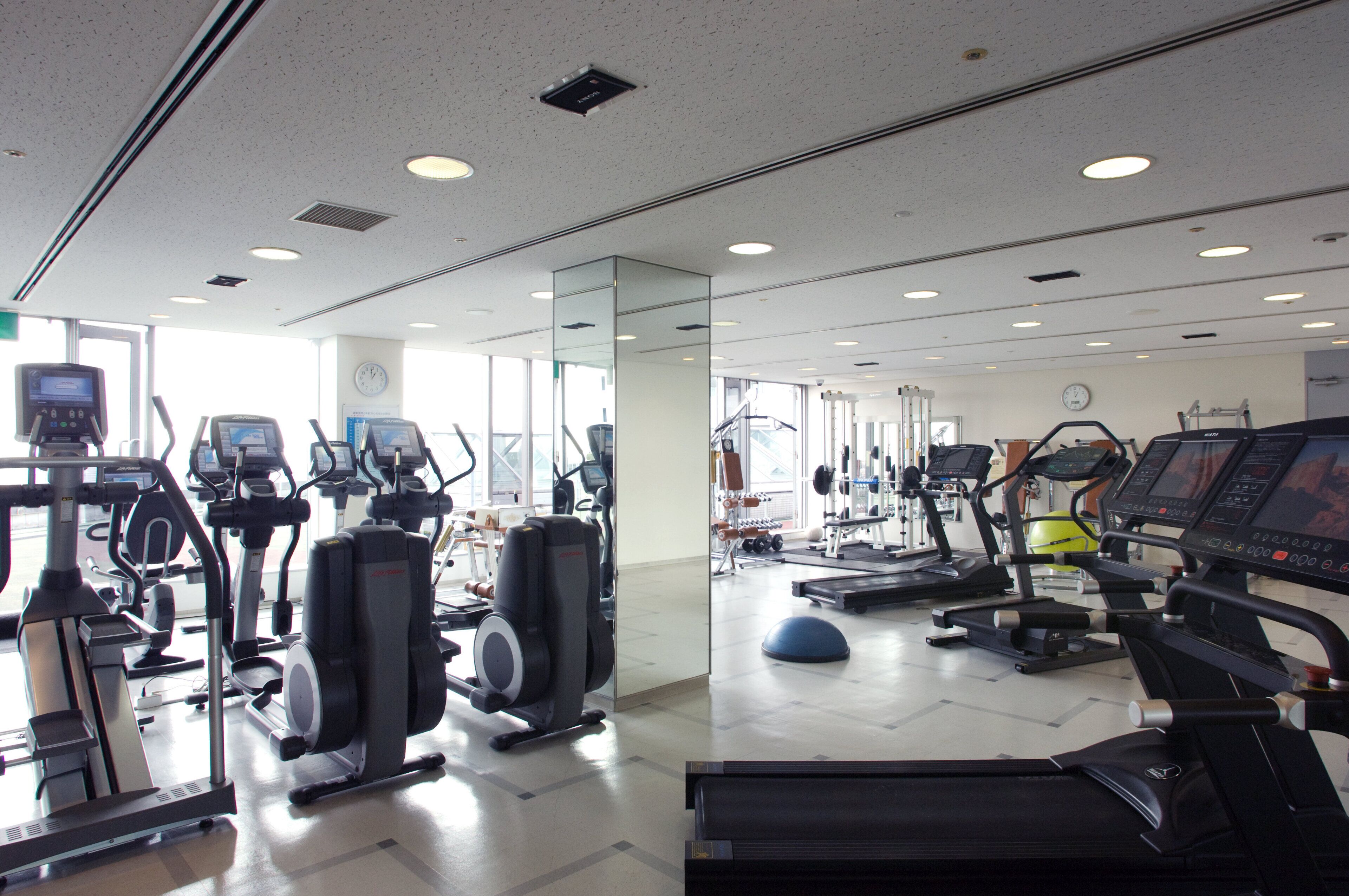 Une salle de sport équipée de divers appareils d’exercice, notamment des tapis de course, des vélos d’appartement et des appareils de musculation.