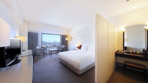 A hotel room with a bed, a desk with a TV, a chair, a desk lamp, a window with a city view, and a bathroom with a mirror and sink. - ANA Crowne Plaza Kobe by IHG (Kobe)