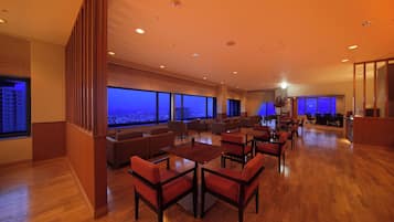 Un amplio vestíbulo de hotel con techo alto, ventanas grandes que ofrecen vistas de la ciudad y una zona de estar moderna con mesas y sillas.