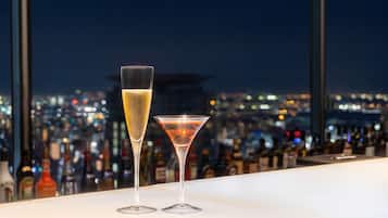 Two glasses of beverages on a bar counter with a cityscape view in the background.