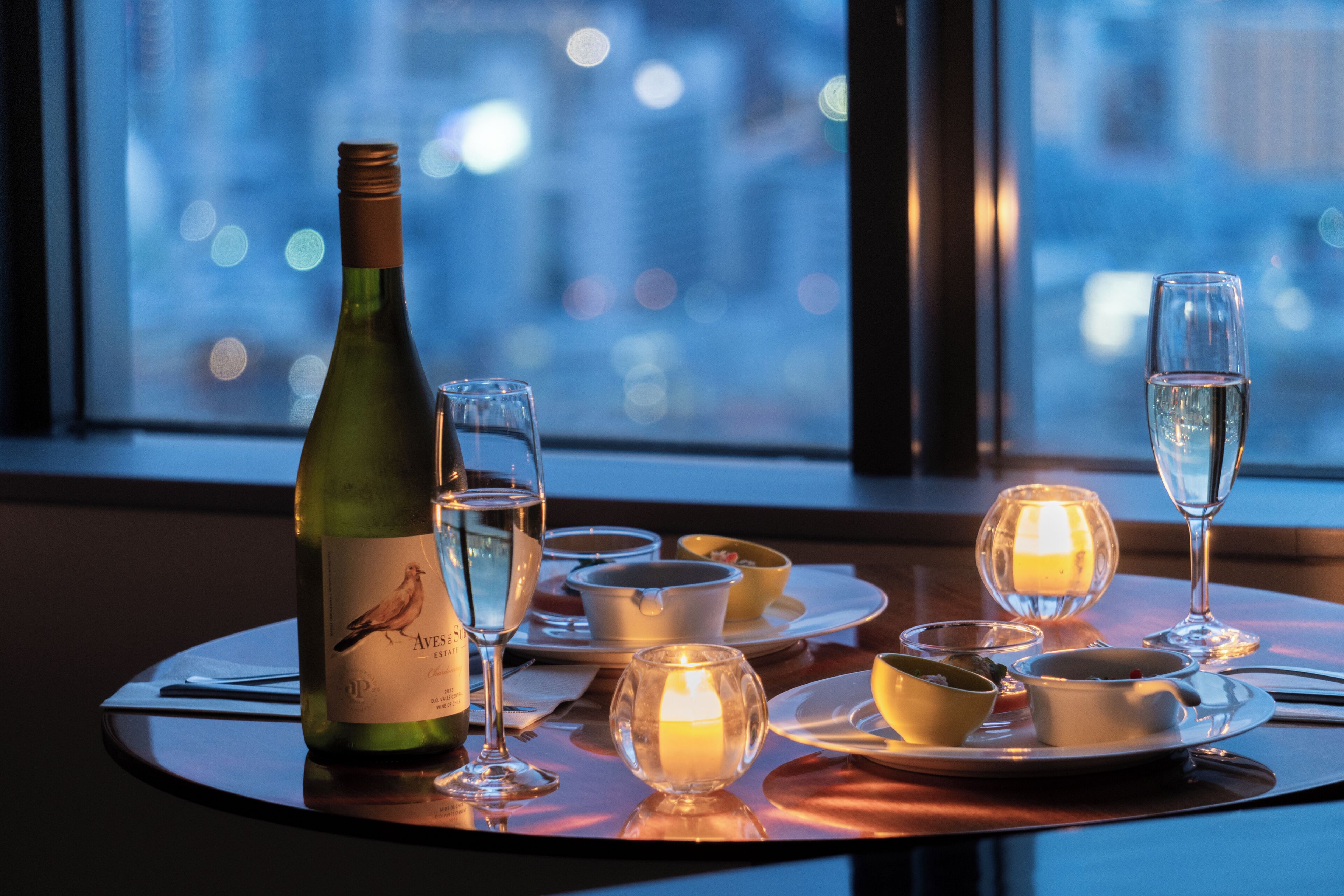 A table set for dining with a bottle of wine, glasses, and candles.