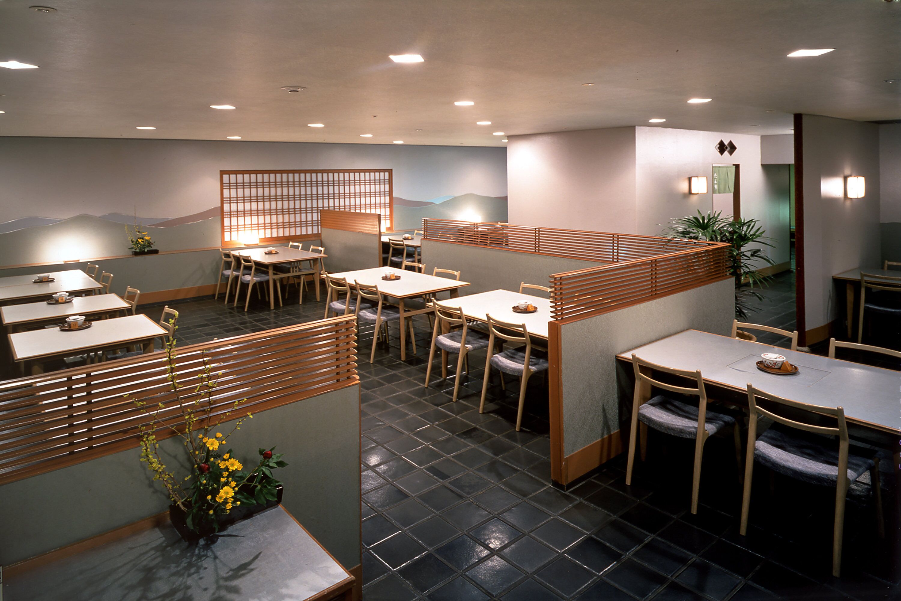 A restaurant with multiple tables and chairs, wooden partitions, and a mural on the wall.