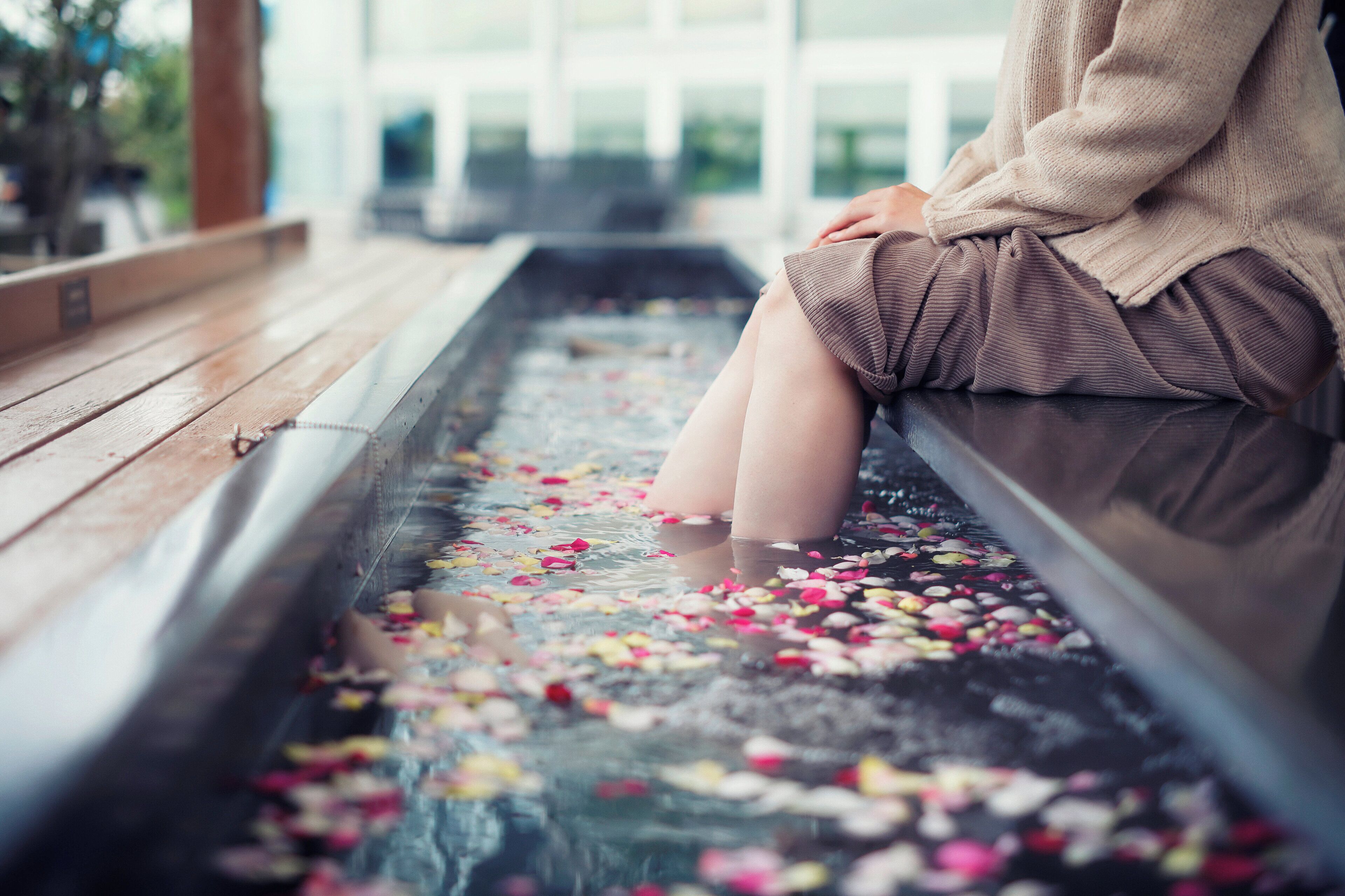 A person sitting by a water feature with floating flower petals.