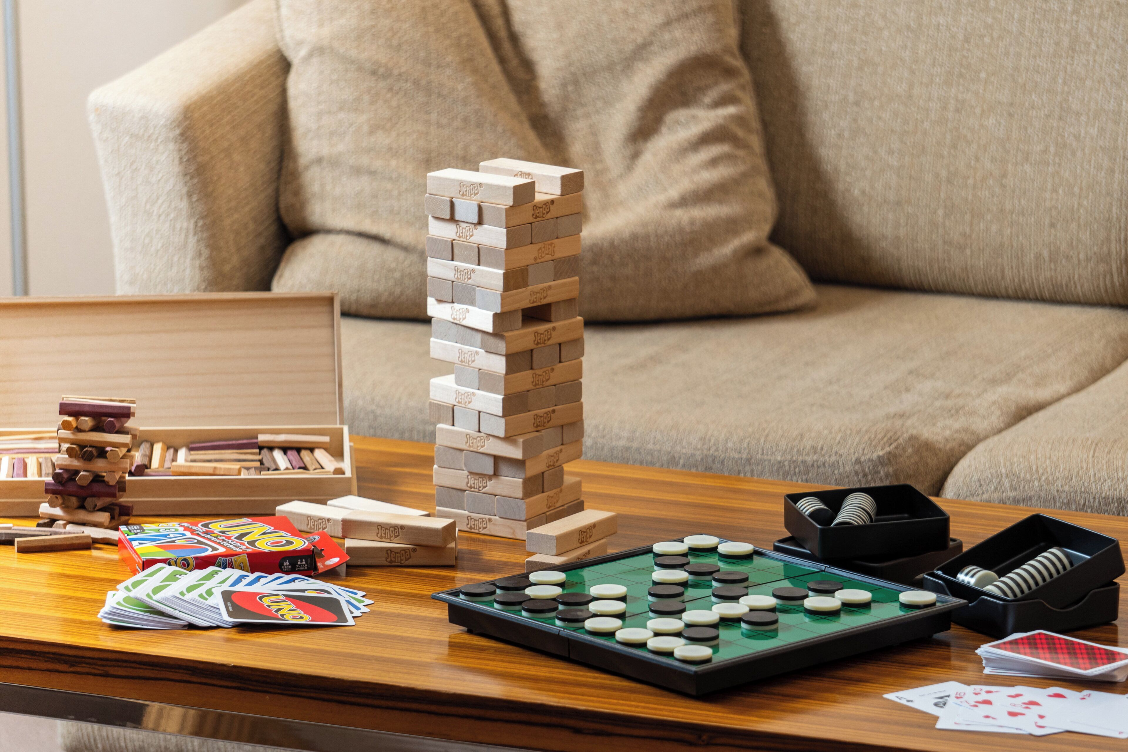 A wooden block tower, dominoes, and a checkered board game on a wooden table.